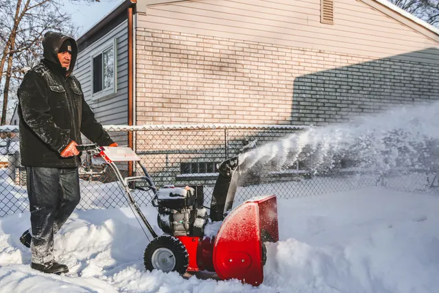 A man pushing a snow blower in his driveway